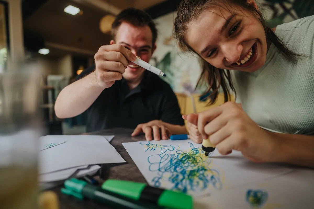 A teenage girl and boy playing with markers laughing