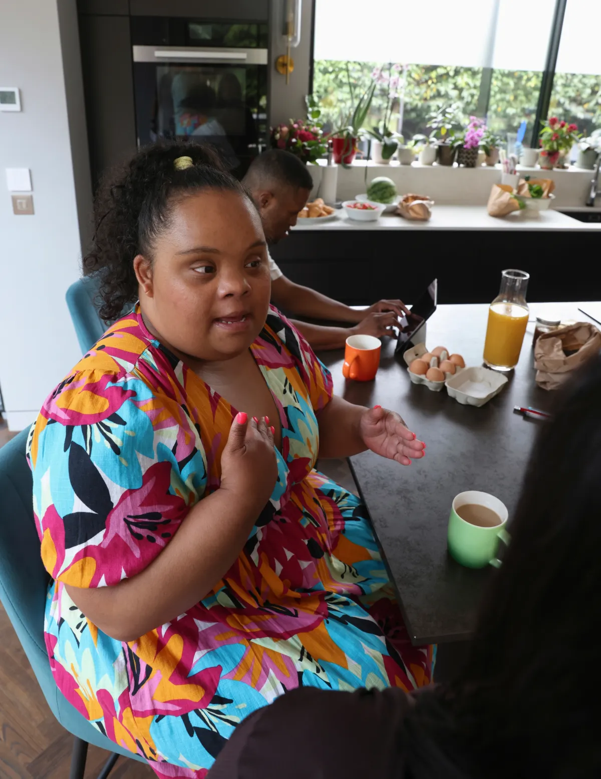 Young woman with Down syndrome talking while sitting in modern kitchen